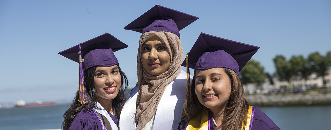 3 graduating students posing at Commencement